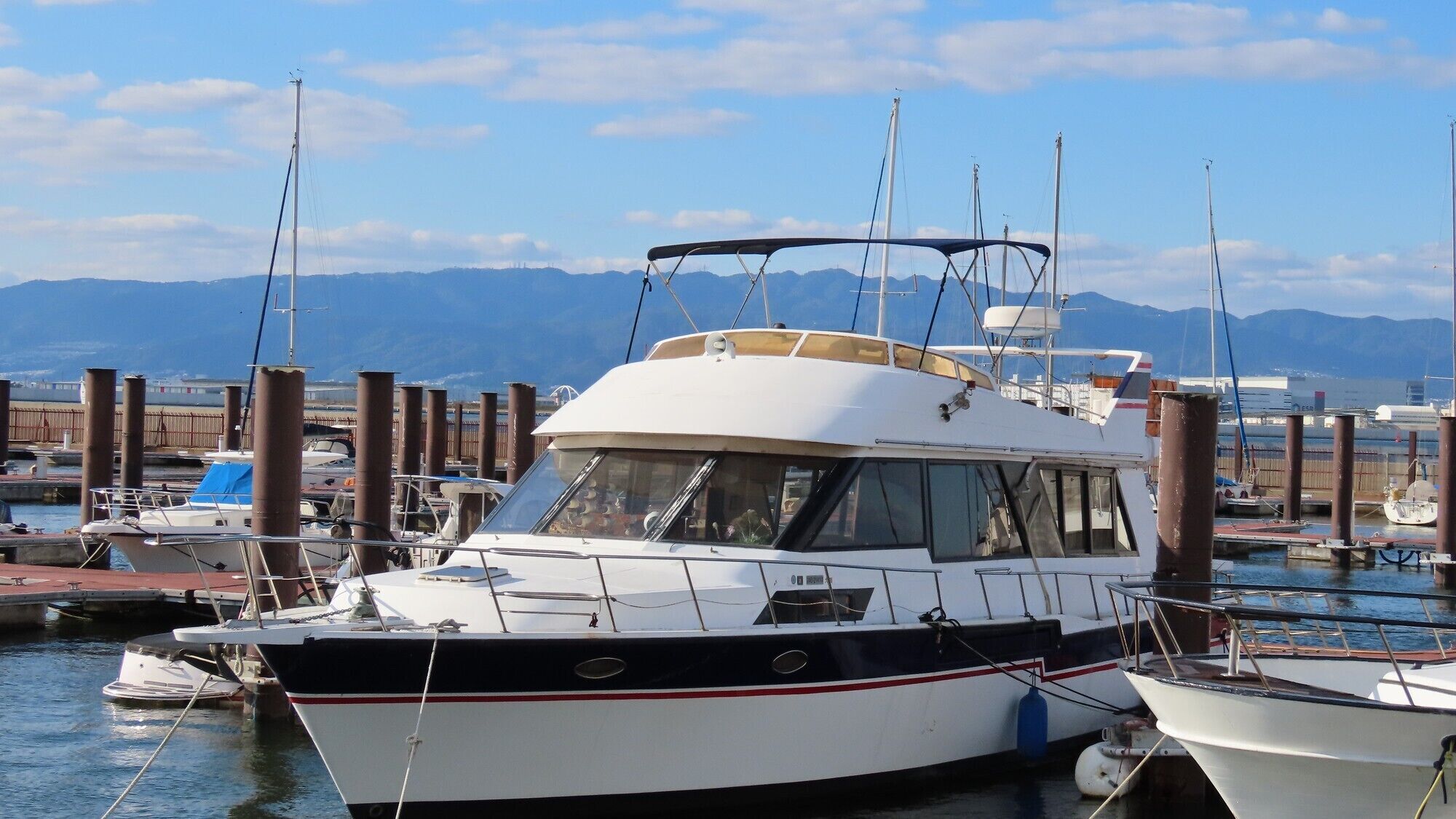 Un port de plaisance avec des bateaux amarrés, un ciel dégagé et des montagnes en arrière-plan.