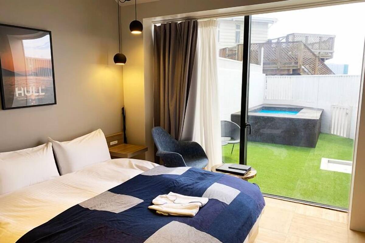 Une chambre d’hôtel avec un lit, une chaise, une petite table et une vue sur une piscine extérieure.