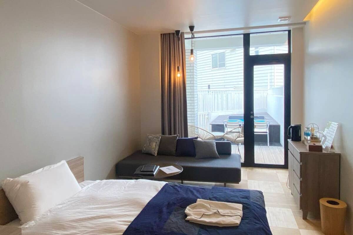 Une chambre d’hôtel moderne dotée d’un grand lit, d’un canapé-lit, d’un bureau et offrant une vue sur le balcon extérieur.