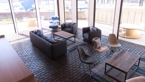 Un espace de détente intérieur moderne, doté de canapés, de fauteuils et de tables, et de grandes fenêtres offrant une vue sur l’extérieur.