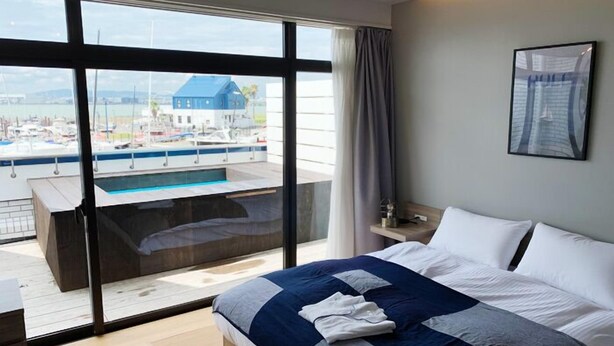 Une chambre d’hôtel moderne dotée d’un grand lit, offrant une vue sur un port de plaisance, et comprenant un petit espace piscine.