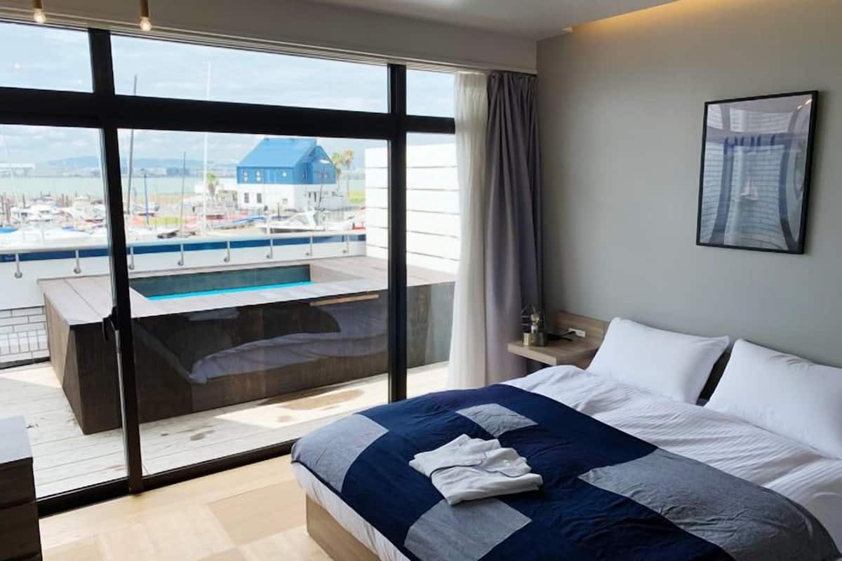 Une chambre d’hôtel moderne dotée d’un grand lit, offrant une vue sur un port de plaisance, et comprenant un petit espace piscine.