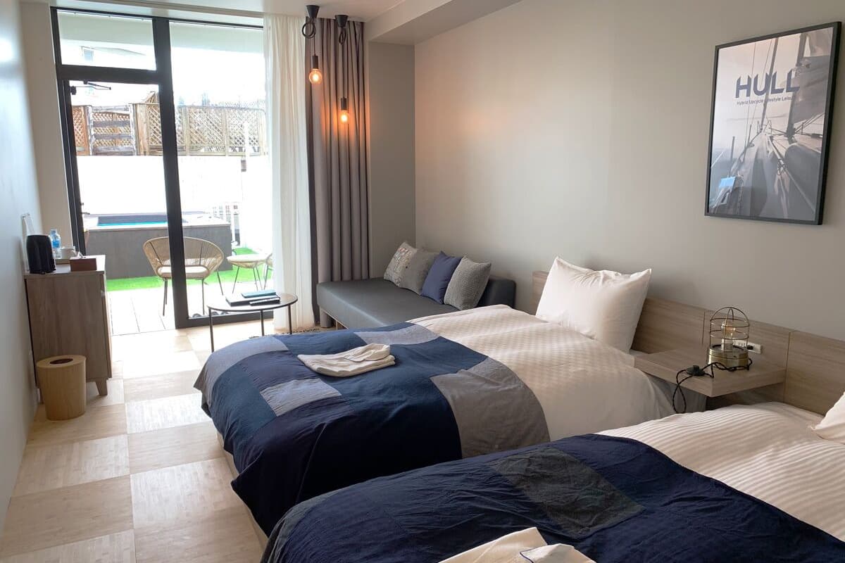 Une chambre d’hôtel avec deux lits, un petit bureau, une chaise et une vue sur l’extérieur.