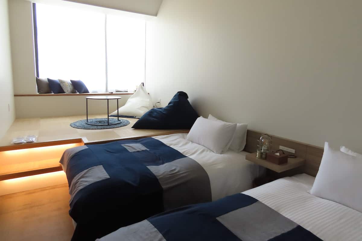 Ein modernes Hotelzimmer mit zwei Betten, einem kleinen Tisch und einer Sitzecke am Fenster.