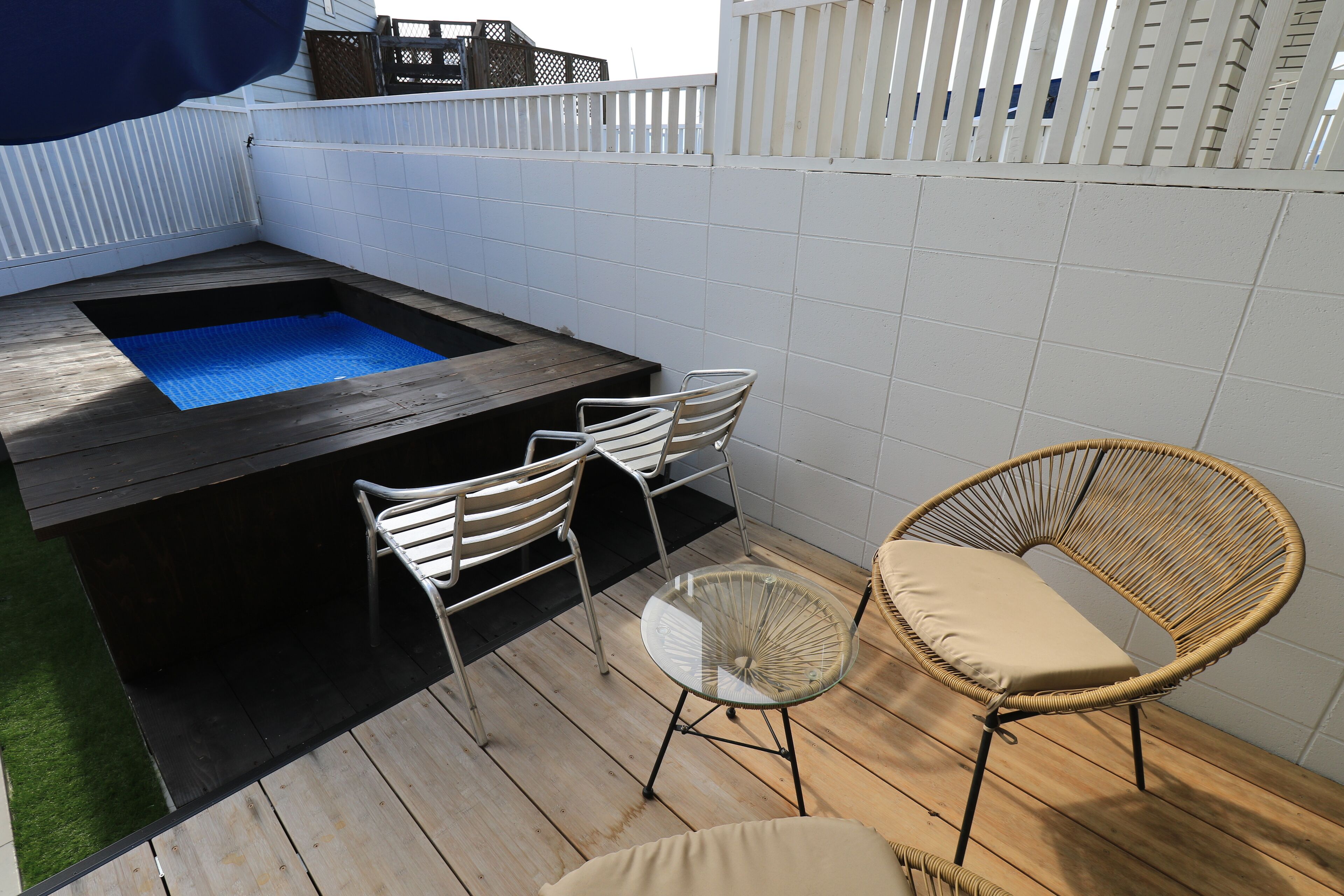 A wooden deck with a hot tub, white chairs, and a wicker chair.