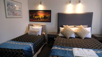 A hotel room with two beds, each with patterned bedding and pillows, a nightstand, a framed picture on the wall, and a painting above the beds.