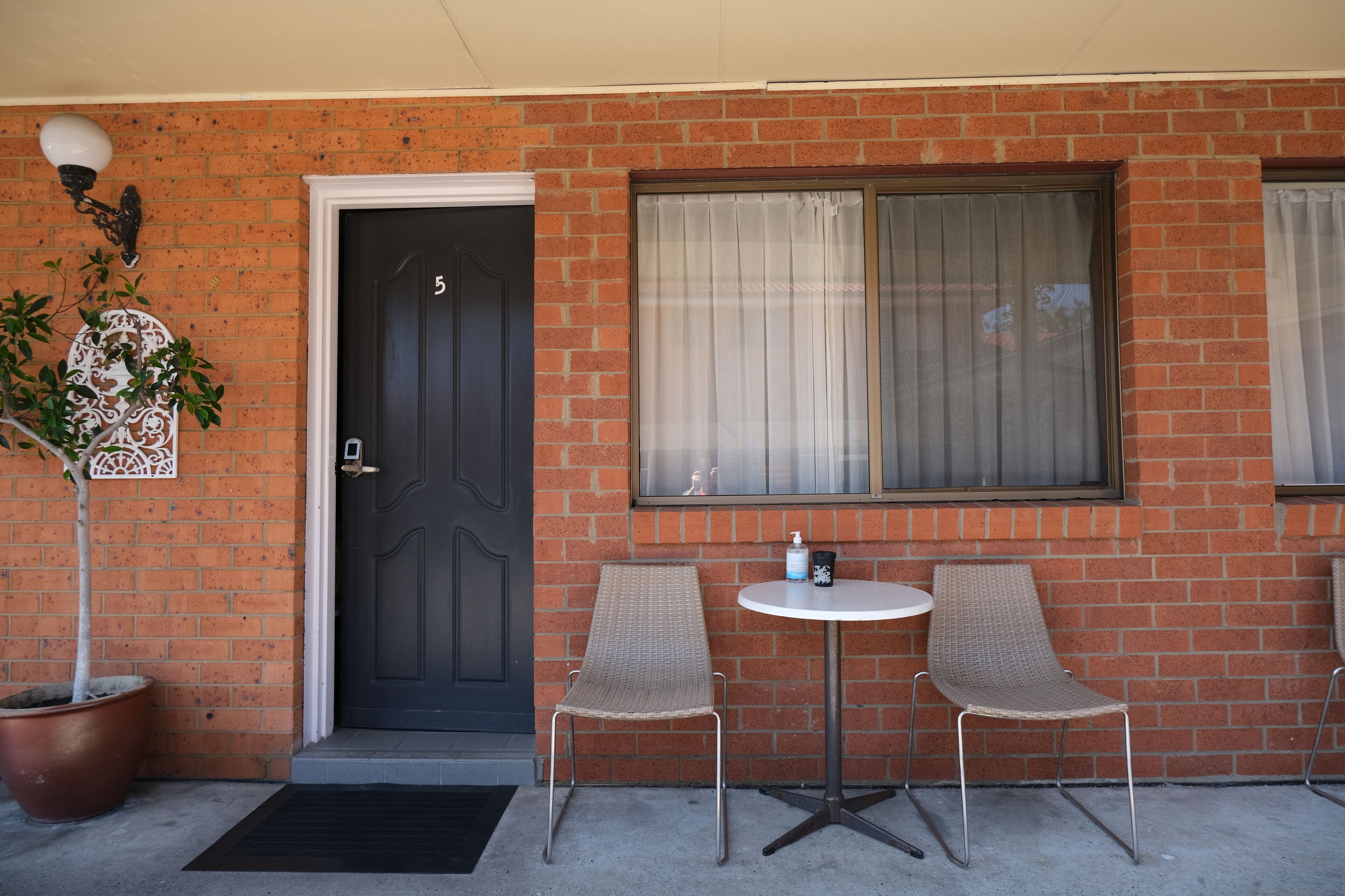 A brick building with a black door, two wicker chairs, a small round table, and a potted plant.