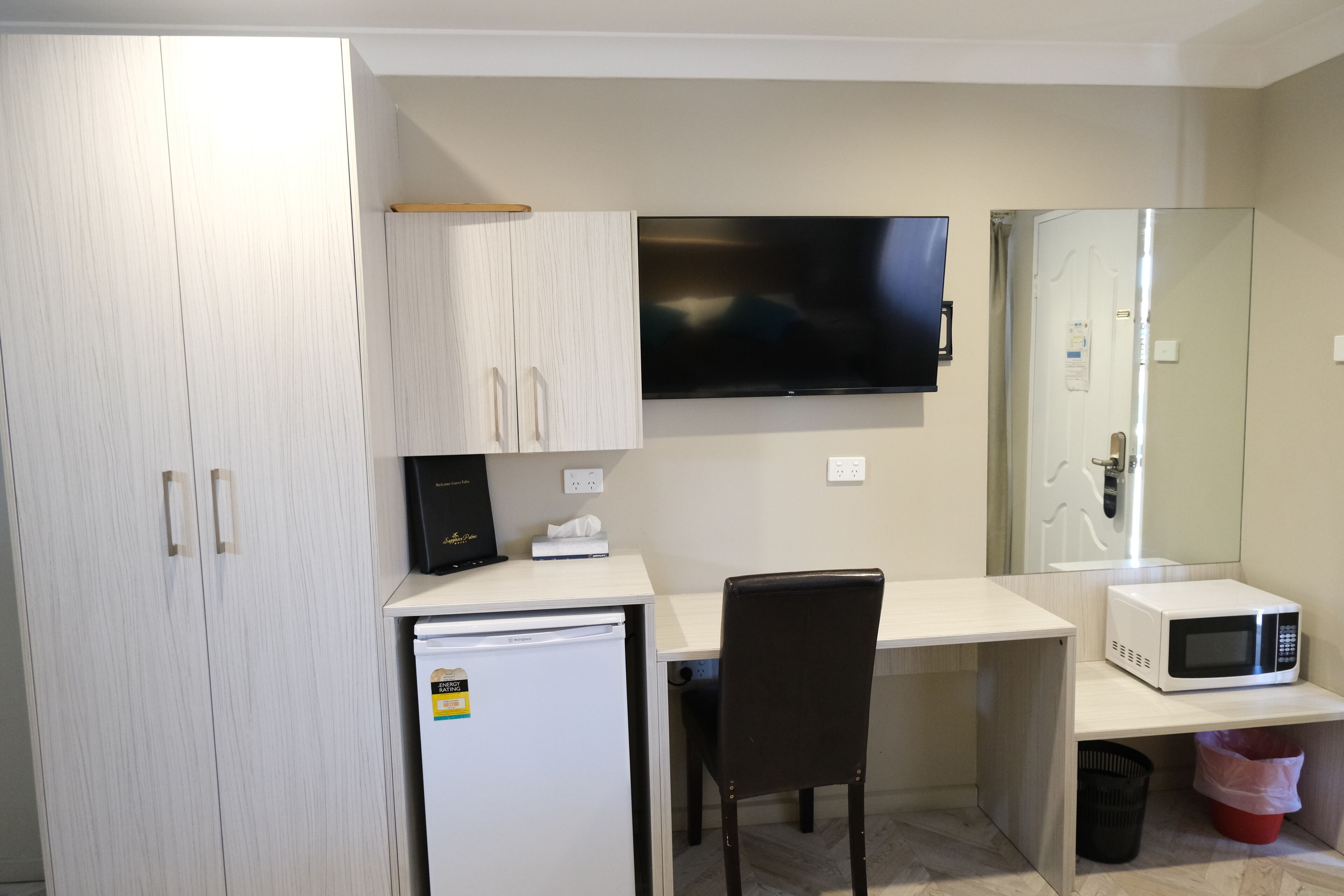 Una kitchenette compacta con refrigerador, microondas y televisor de pantalla plana montado en la pared.