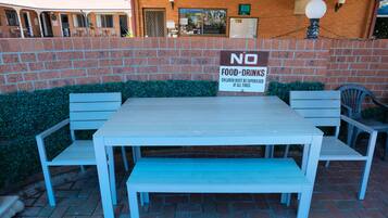 Een terras met een tafel en bankjes, een bakstenen muur en een bordje met de tekst 'GEEN ETEN EN DRINKEN'.