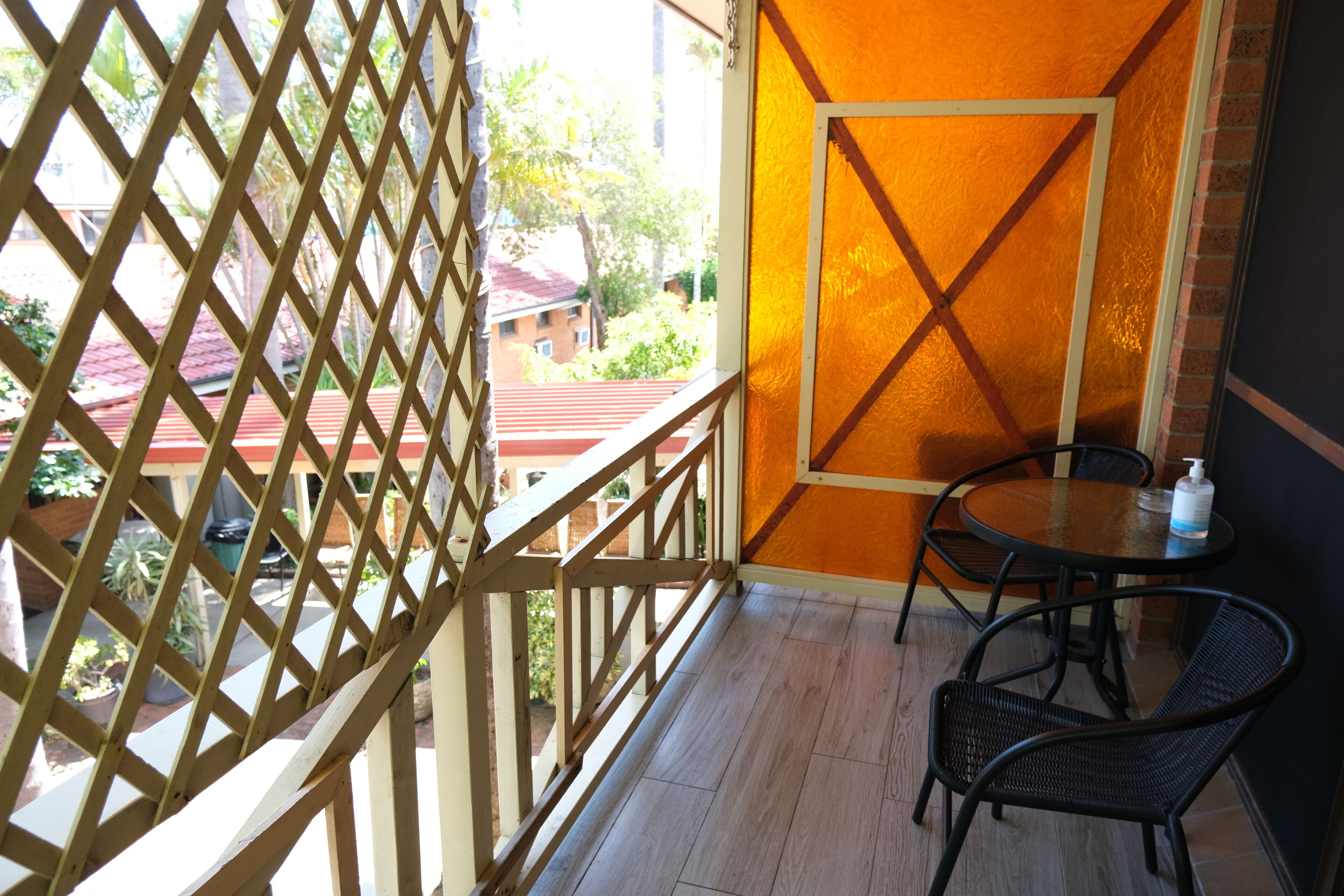 A balcony with a wooden lattice, a round table with chairs, and a view of buildings and trees.