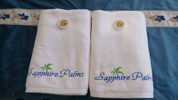 Two white towels with embroidered text and a logo, placed on a blue fabric with a floral pattern.