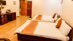 Habitación de hotel con dos camas, un escritorio, una silla, una mesita con una botella y flores, y una puerta que da a otra habitación.