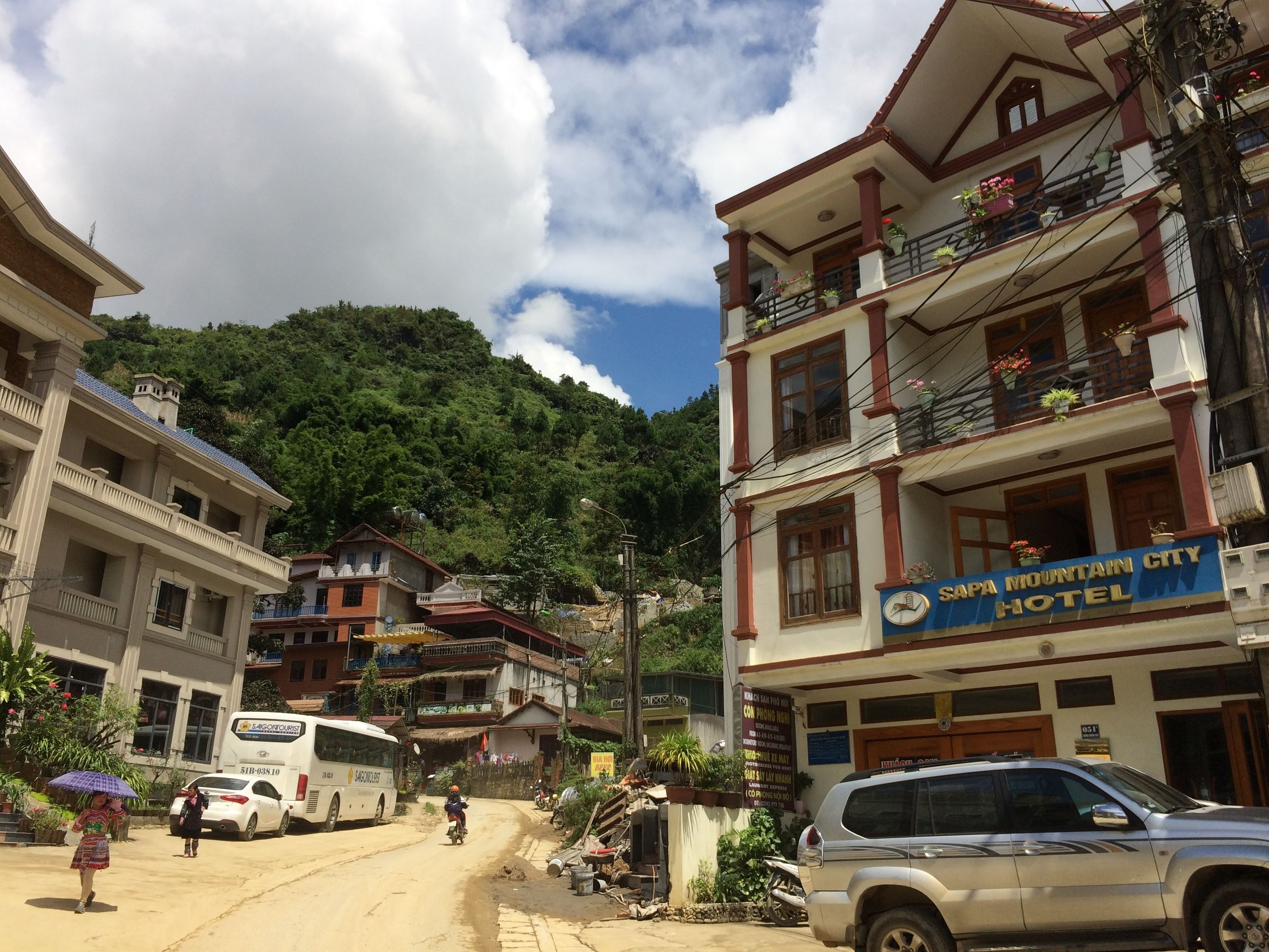 A hotel with a signboard, a building with balconies, and a mountainous backdrop.