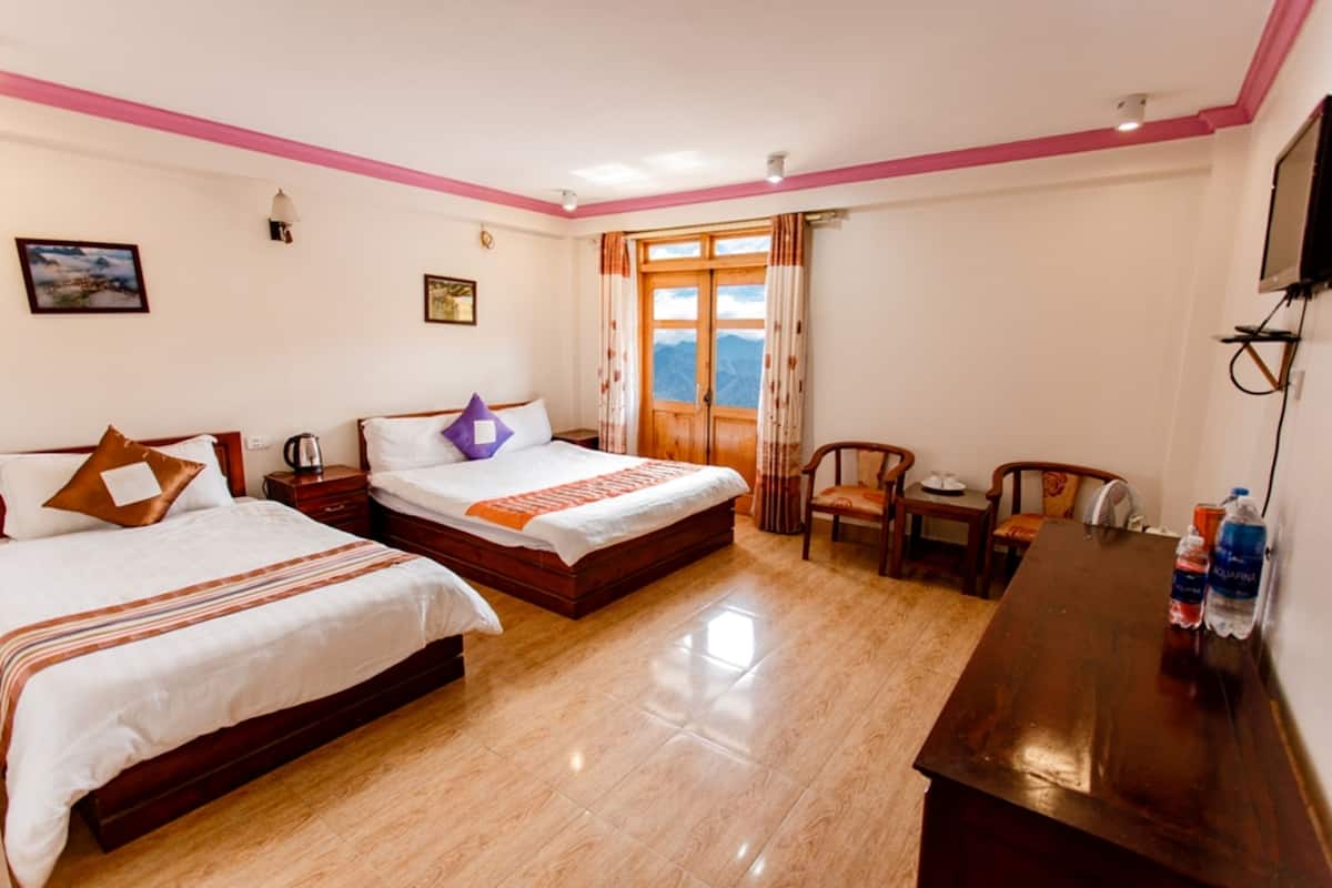 Una habitación de hotel con dos camas, un escritorio de madera, una silla y un ventanal con cortinas.