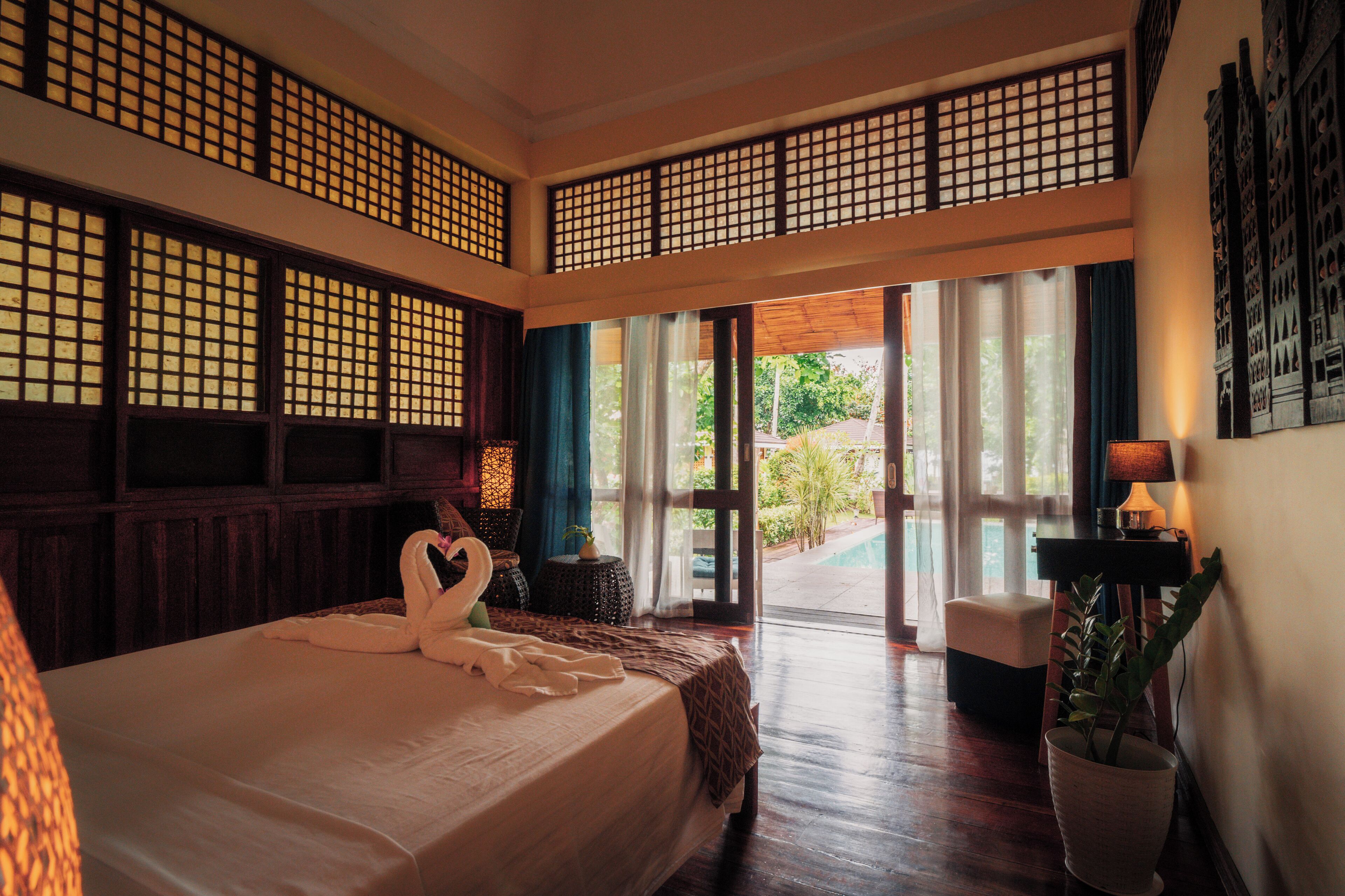 A hotel room with a large bed, a view of the garden, and a traditional wooden partition.