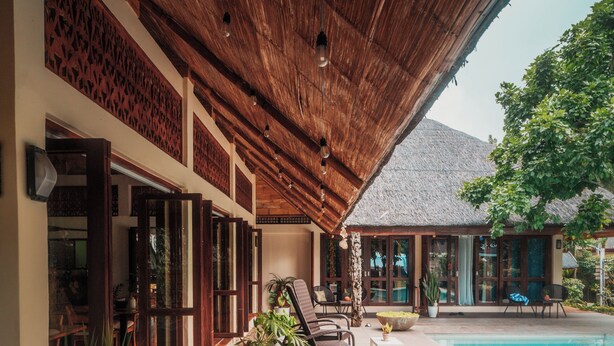 Un espacio exterior cubierto con piscina, piso de madera, plantas en macetas y mobiliario.