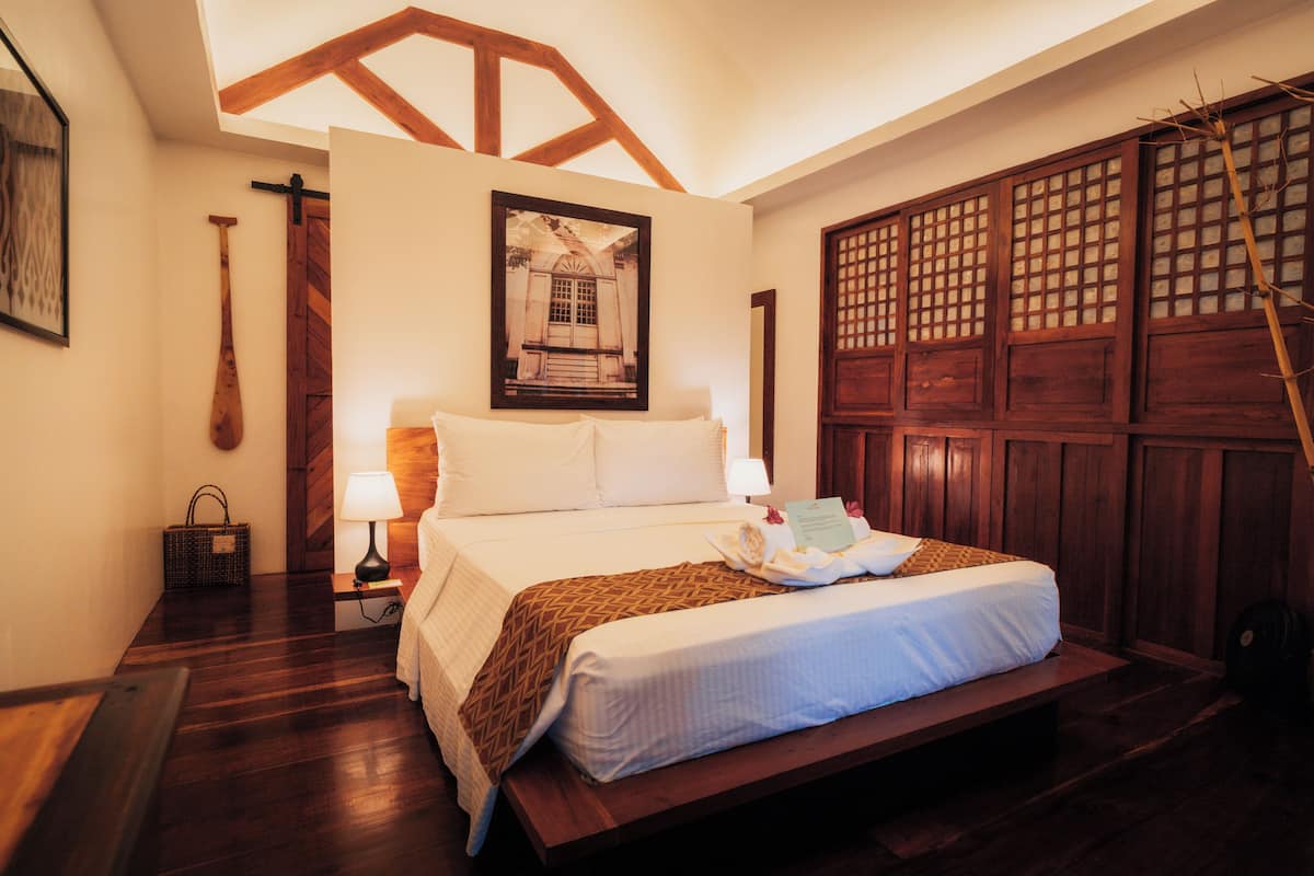 Una cama bien hecha con cabecera de madera, una lámpara de noche y un cuadro en la pared.