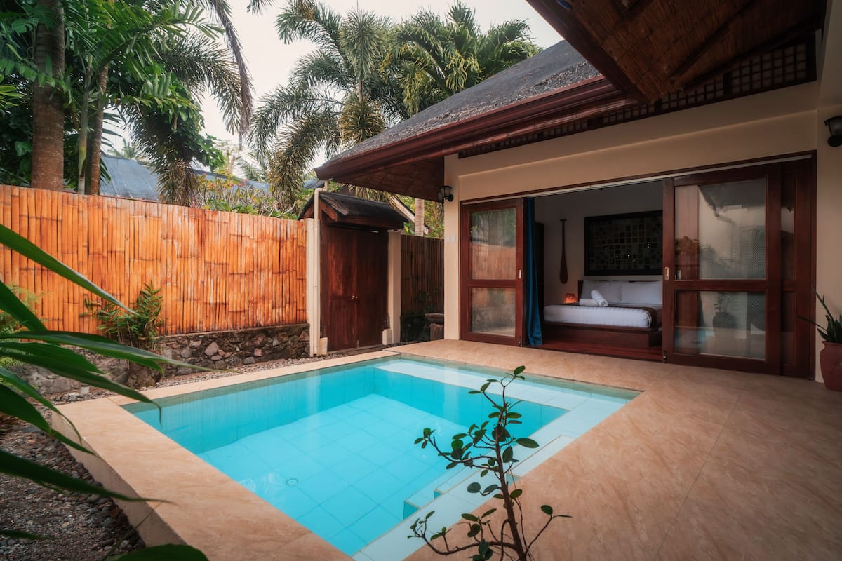 Una piscina con cubierta de madera, un ventanal corredero que da a un dormitorio y una valla de bambú.