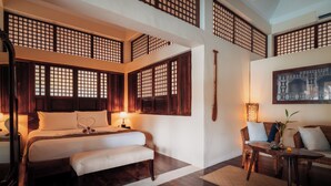 Un dormitorio de estilo tradicional con cama, mesita de noche, banco y un rincón de estar con mesa y sillas.