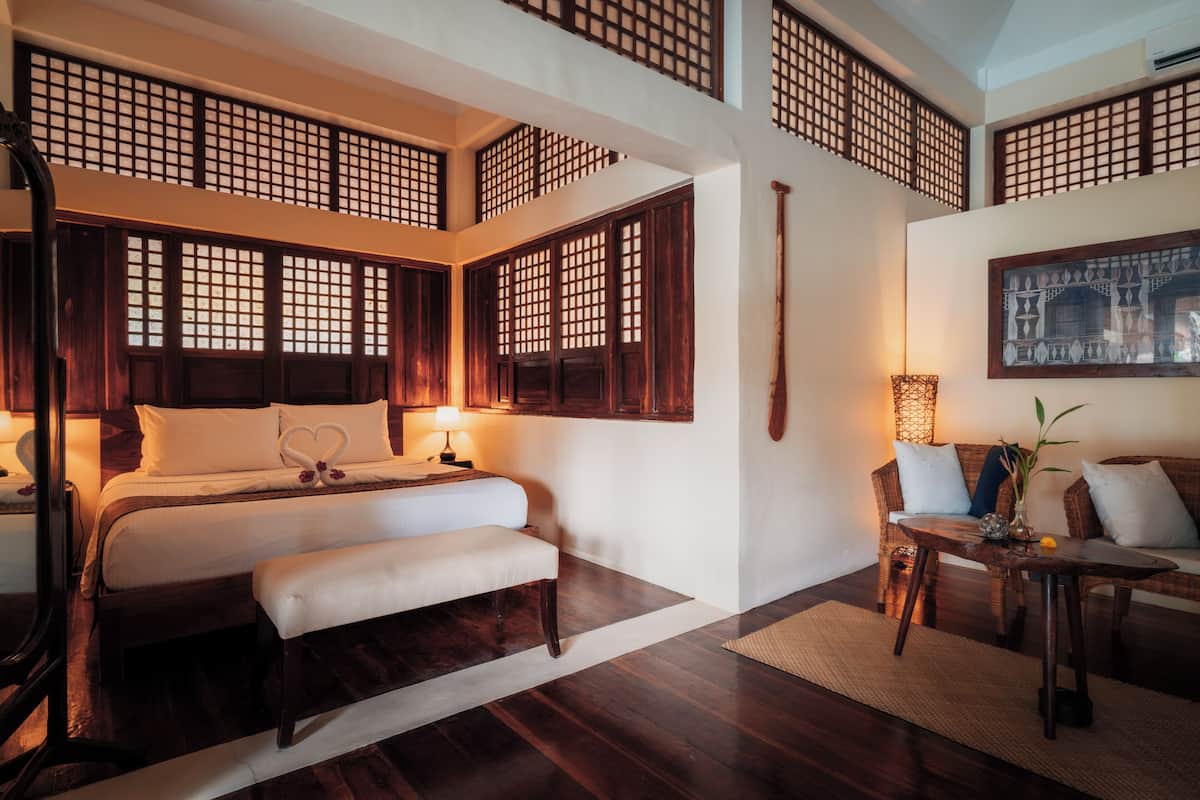 Un dormitorio de estilo tradicional con cama, mesita de noche, banco y un rincón de estar con mesa y sillas.