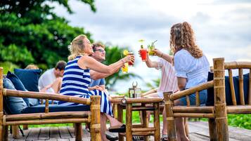 Une terrasse en bois avec des meubles en bambou et une petite table sur laquelle sont disposées des boissons.