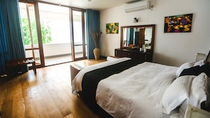 A bedroom with a large bed, a desk, a chair, a ceiling fan, and a sliding glass door leading to a balcony. - Kixi Beach (Unawatuna)