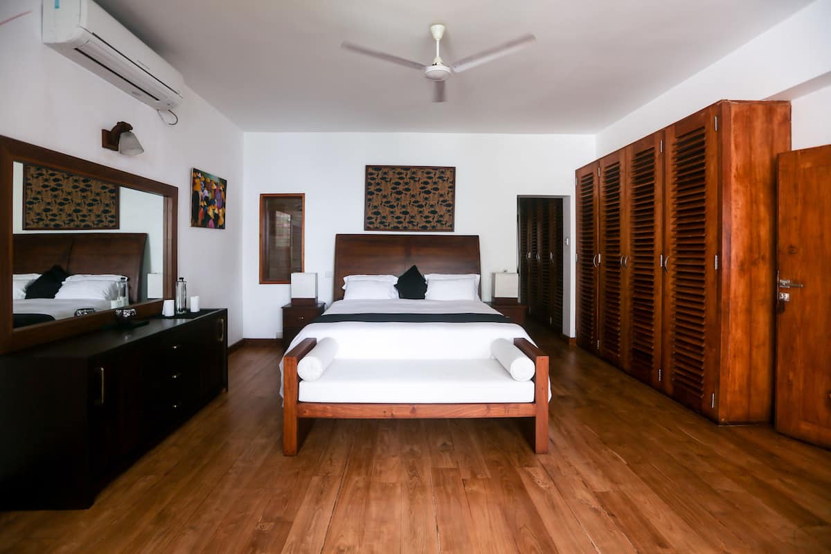 A spacious bedroom with a large bed, wooden wardrobe, and a ceiling fan.