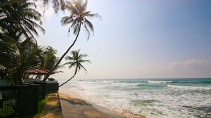 A beach with palm trees, a wooden boat, and ocean waves. - Kixi Beach (Unawatuna)