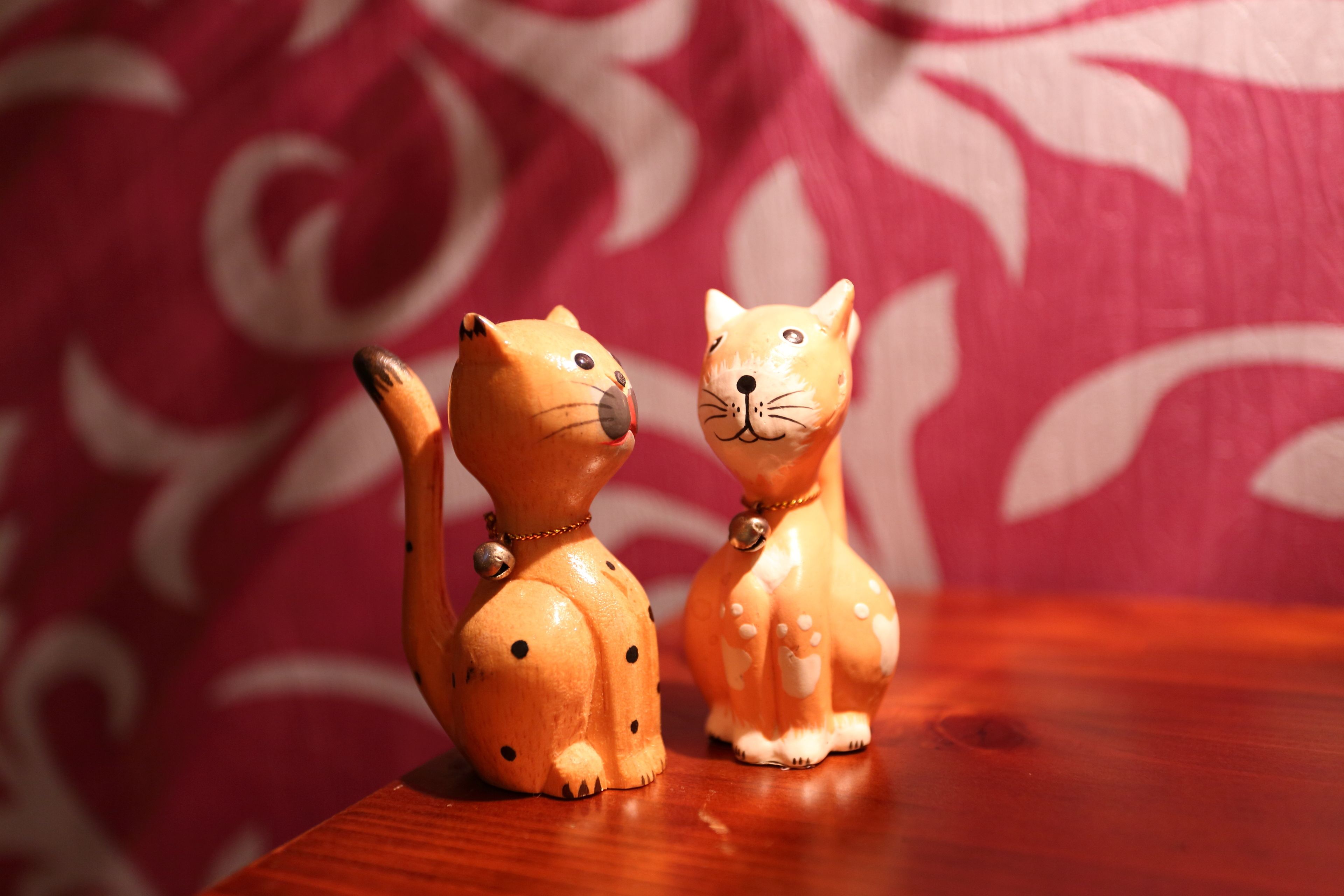 Two ceramic cat figurines on a wooden surface with a patterned red background.
