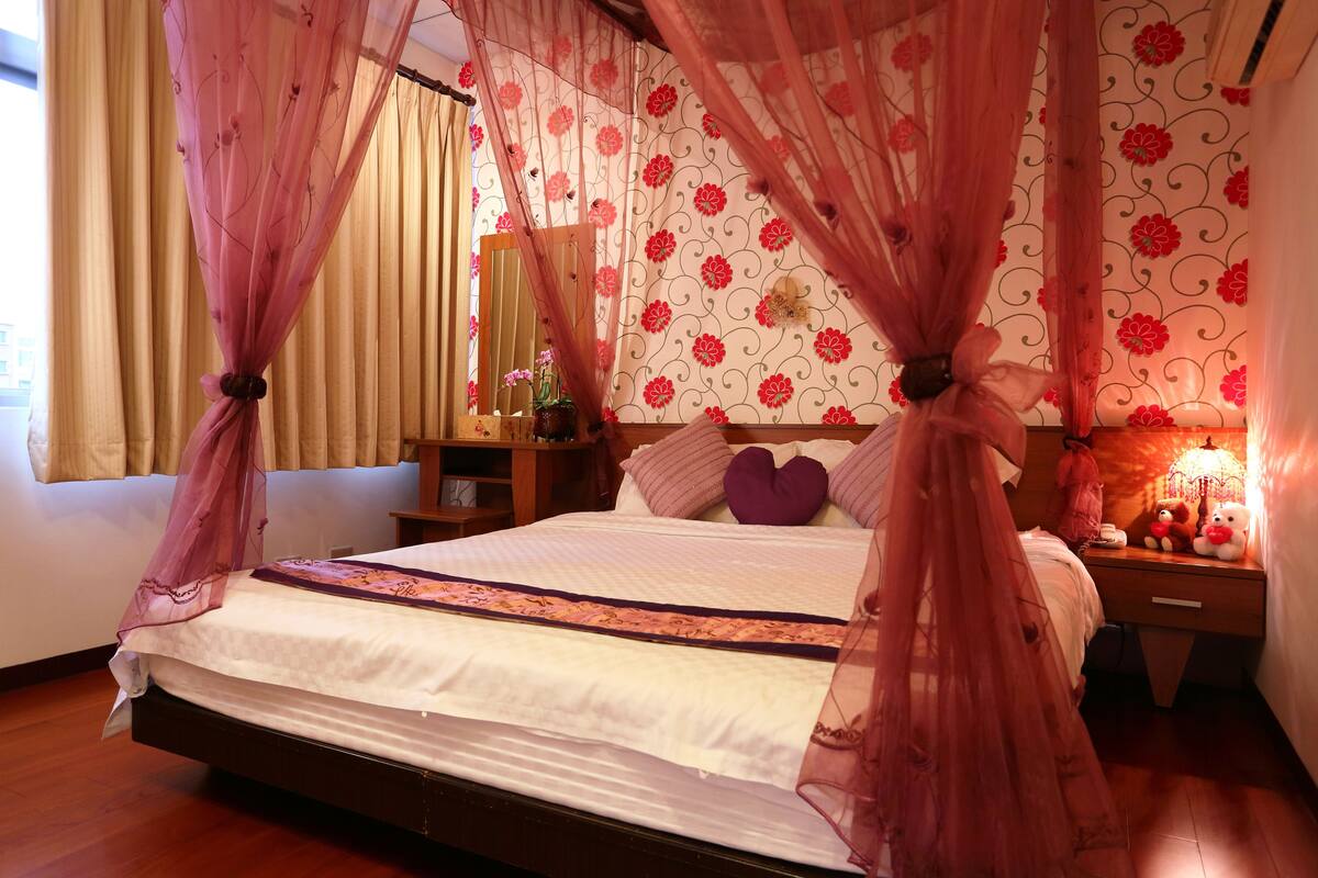 A bedroom with a bed, a nightstand, a lamp, and a window with curtains.