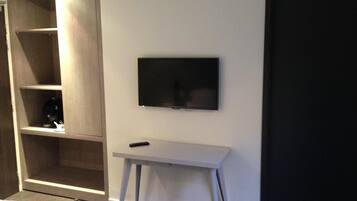 Een hotelkamer met een bed, een aan de muur bevestigde televisie, een klein tafeltje en een kledingkast.