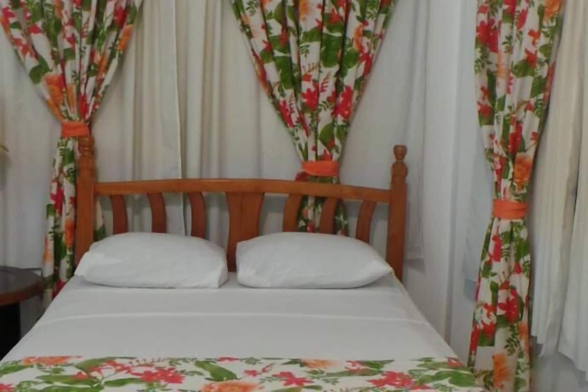 A bed with white linens and a floral bedspread, flanked by curtains with a tropical print.