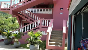 A pink building with a staircase, potted plants, and a sign indicating an office. - Top Ranking Guesthouse (Speyside)