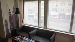 Et værelse med en grå sofa, et lille bord med magasiner og et vindue med persienner.