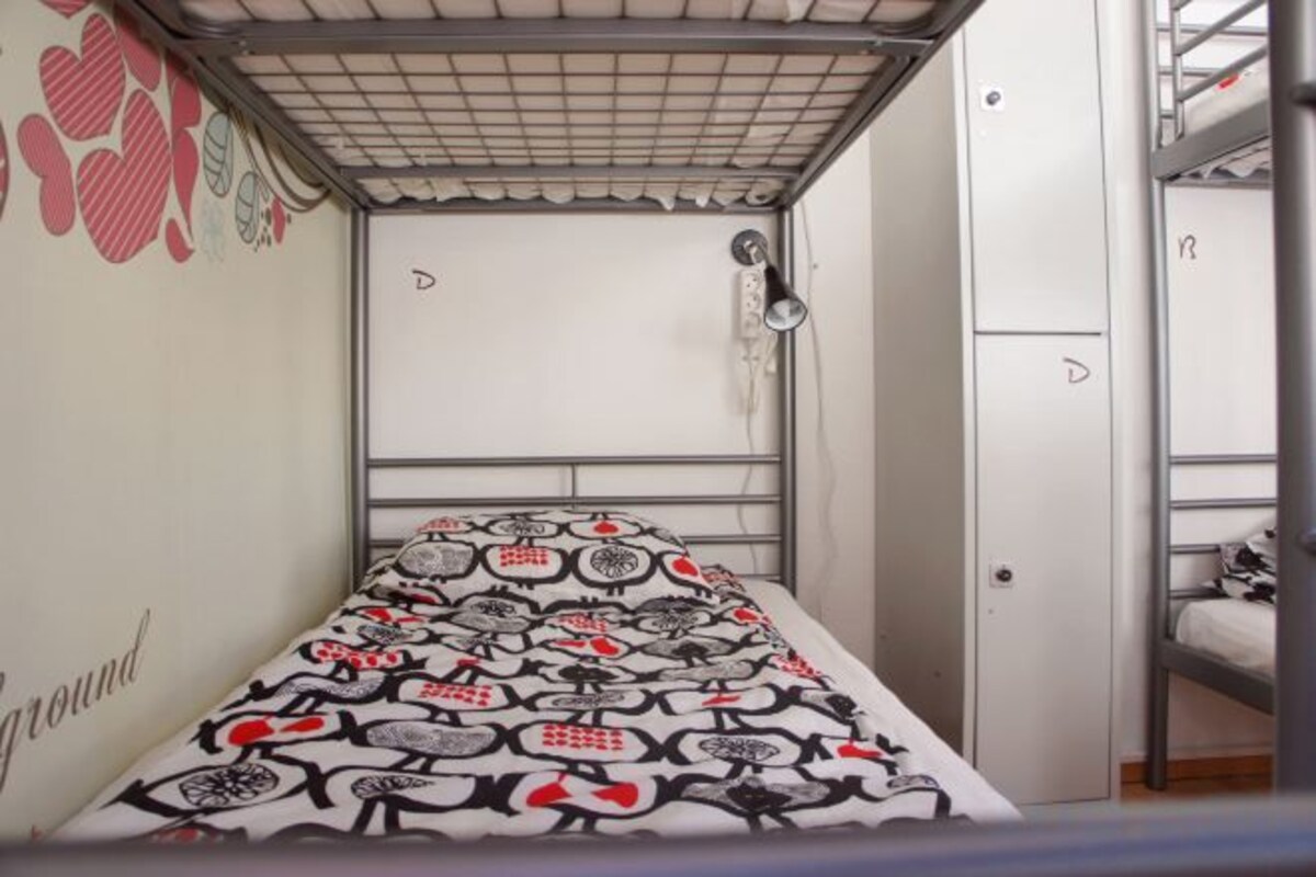 A bunk bed room with a patterned bedspread, a white door, and a metal bunk bed on the right.