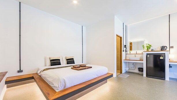 A modern hotel room with a bed, bedside table, and a kitchenette area. - Infinity Guesthouse (Koh Tao)