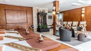 A spacious room with a large wooden panel wall, a stone fireplace, and a seating area with wicker chairs and a massage table. - Infinity Guesthouse (Koh Tao)