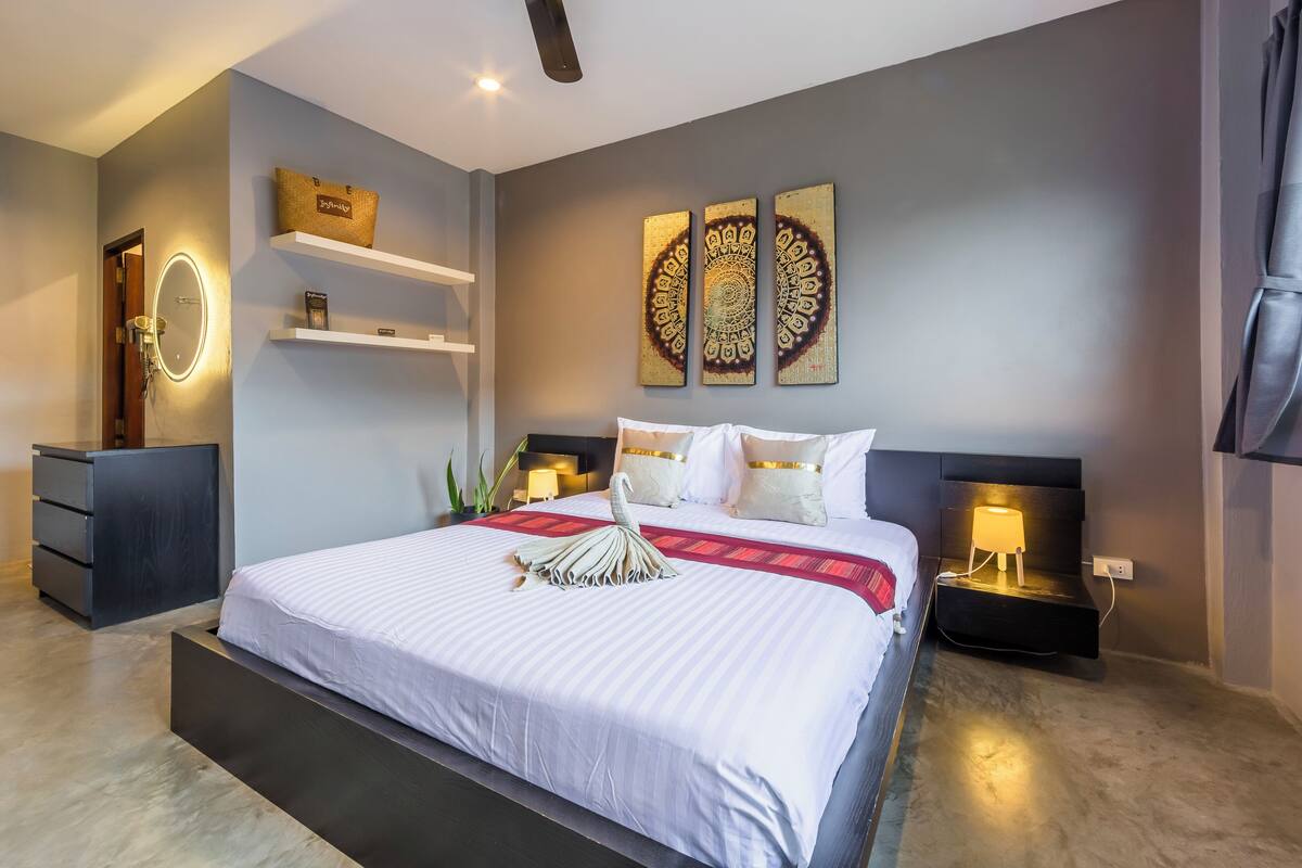 A modern hotel room with a large bed, bedside tables, a mirror, and wall art.