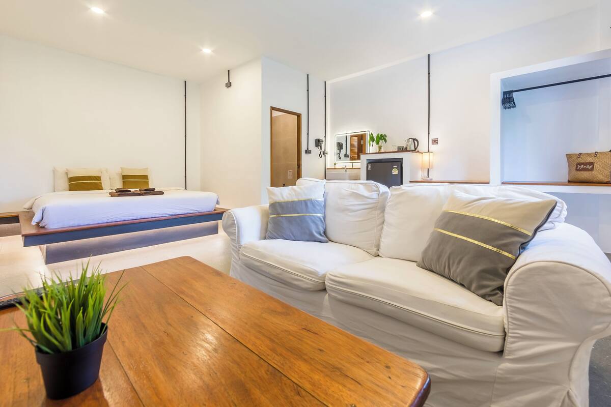 A modern hotel room with a bed, a sofa, a coffee table, and a small plant.
