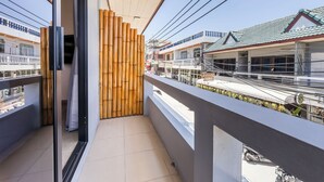 A balcony with a view of a street, bamboo wall, and a building with a green roof. - Infinity Guesthouse (Koh Tao)