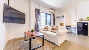 A modern living room with a flat-screen TV, a sofa, a coffee table, and a kitchen area in the background. - Infinity Guesthouse (Koh Tao)