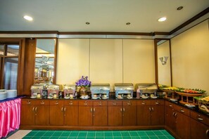 A buffet setup with multiple food dispensers, a decorative vase with purple flowers, and a fruit display. - Phi Phi Hotel (Ko Phi Phi)