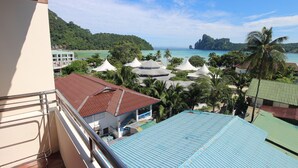 Uitzicht vanaf een balkon op een resort met meerdere gebouwen, een strand en een bergachtige achtergrond.