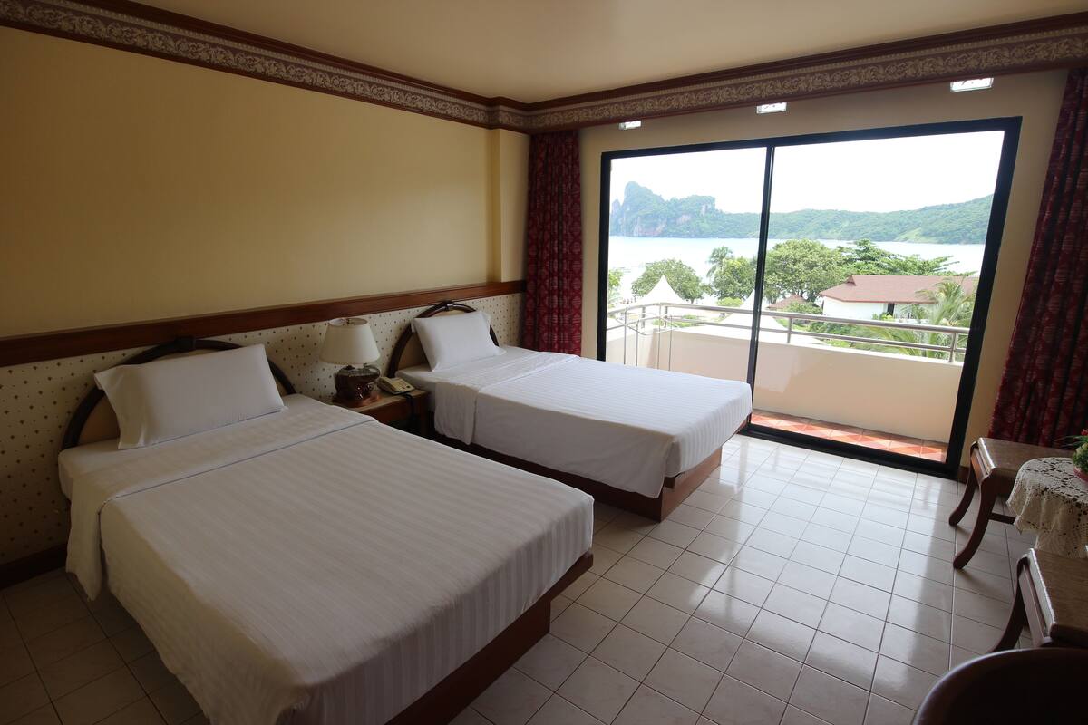 Une chambre d’hôtel avec deux lits, un balcon donnant sur la mer et un coin repas avec une table et des chaises.