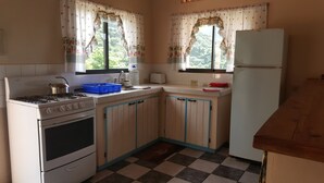 A compact kitchen with a gas stove, oven, and a refrigerator. It features a checkered floor and wooden cabinets with blue trim. - Grand View Guesthouse (Speyside)