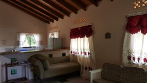 A cozy living room with a sofa, a small table, and a kitchen area with a refrigerator and window. - Grand View Guesthouse (Speyside)