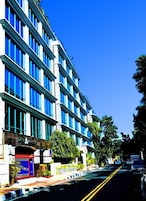 Un edificio de varios pisos con un estilo arquitectónico moderno, que destaca por una serie de ventanas verticales y una entrada principal con un portón azul.