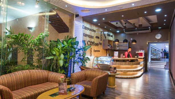 A modern coffee shop interior with seating, a counter, and a staircase in the background. - Hotel Lake Castle (Dhaka)
