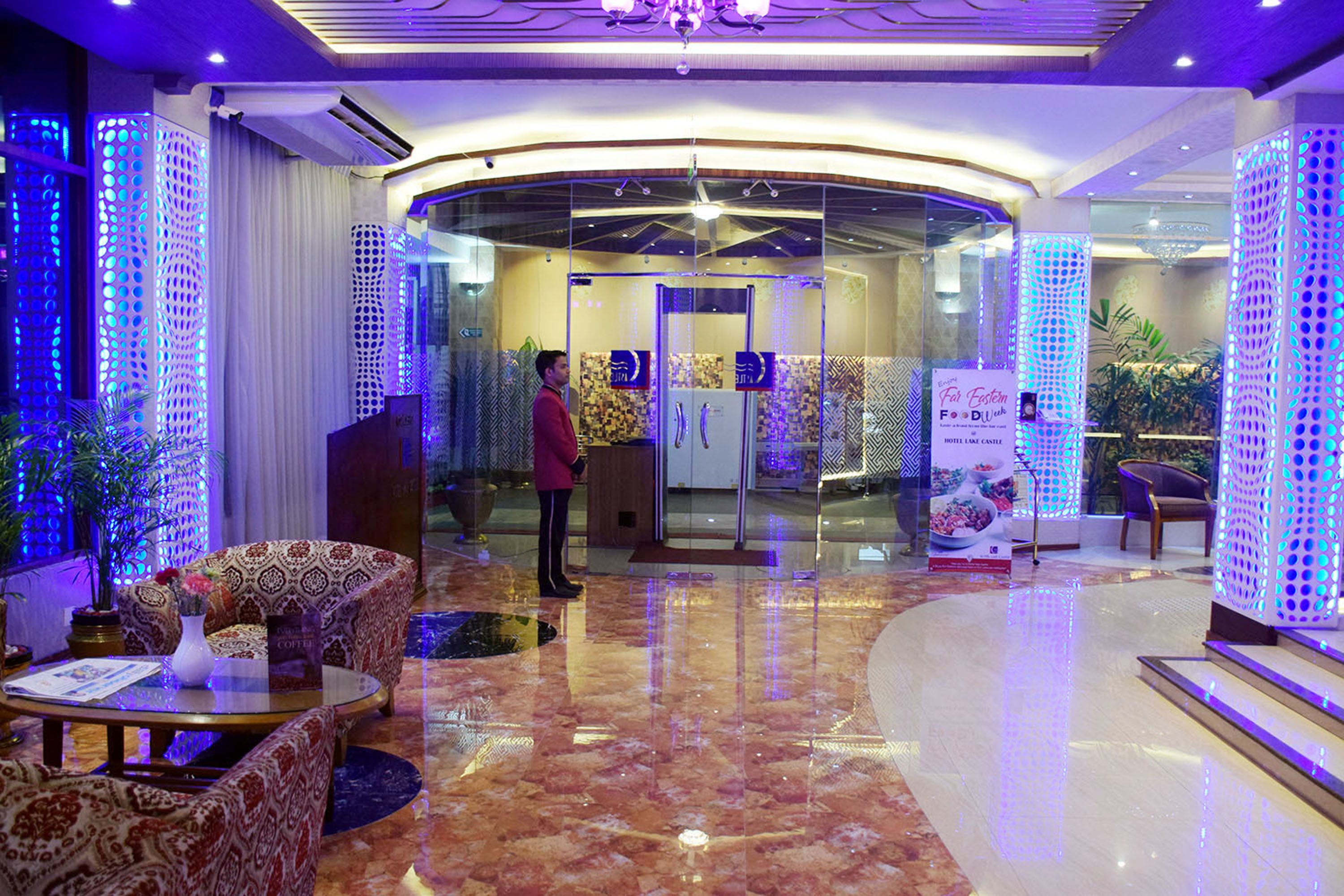 A hotel lobby with a marble floor, patterned sofas, a reception desk, and decorative lighting.