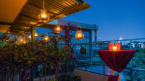 A balcony with hanging lanterns, potted plants, and a table with candles. - Hotel Lake Castle (Dhaka)